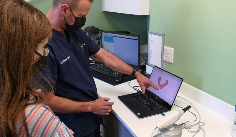 A dentist showing a patient their 3D intraoral scan on screen with the scanner wand on the desk