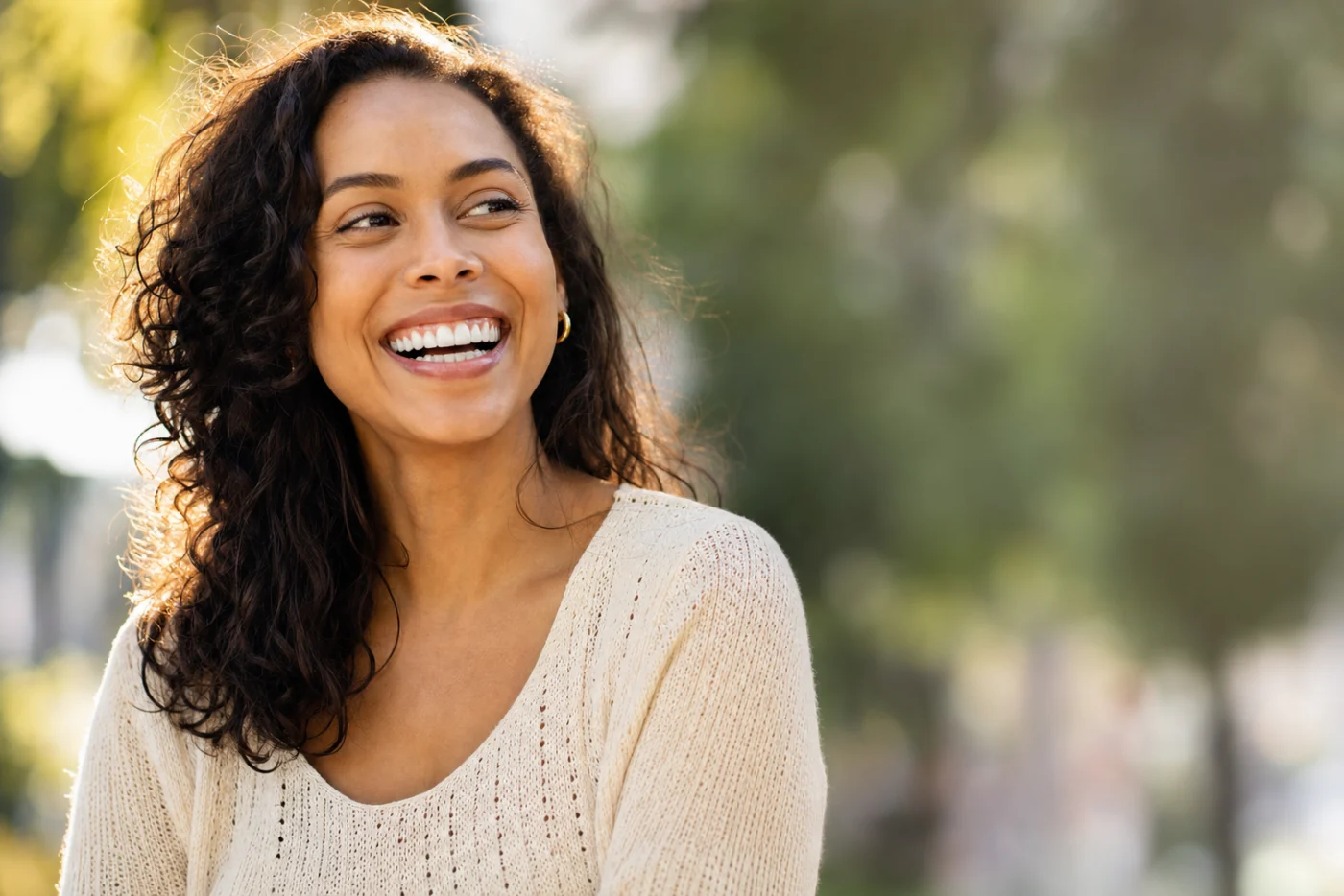 Young woman laughing with a bright, confident, straight smile in warm outdoor light