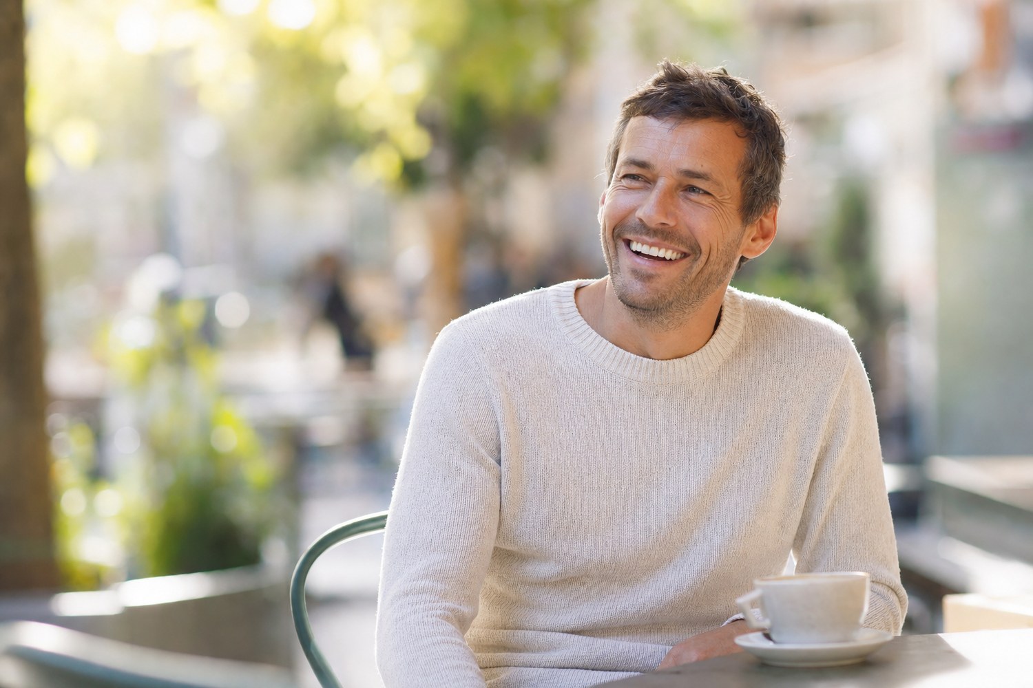 A relaxed man laughing warmly at a sunny outdoor cafe